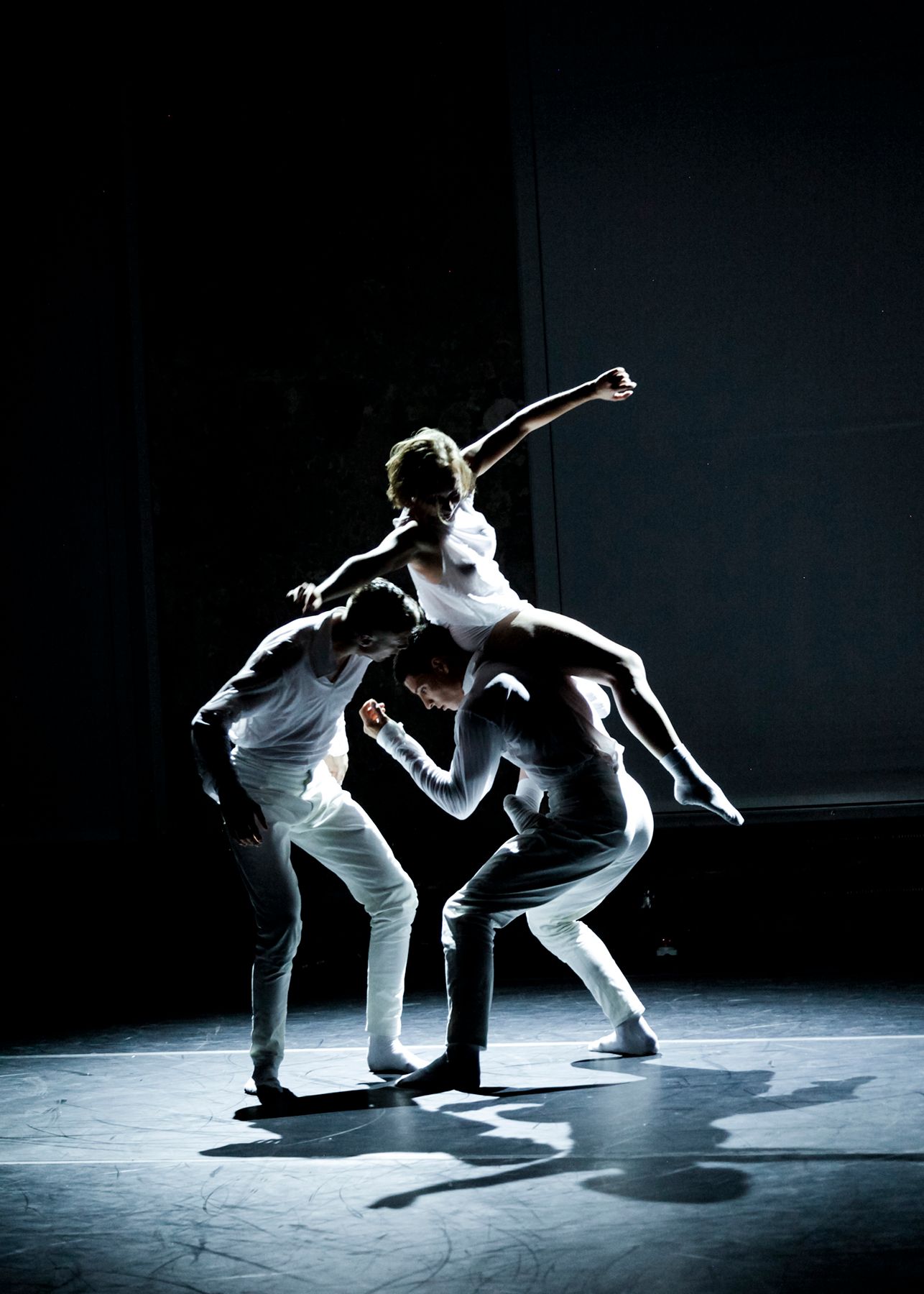 three dancers on a dark stage with spotlight, backlit, dark mood, dancing