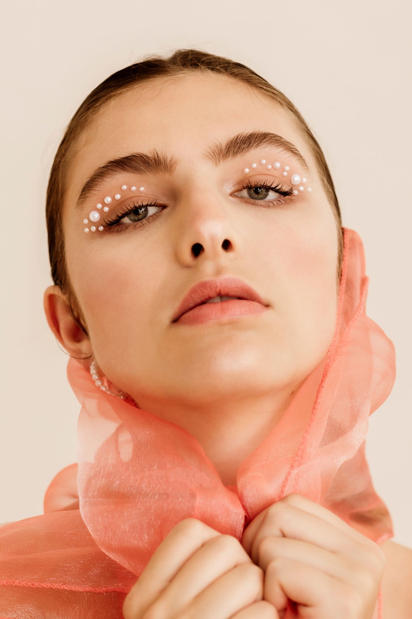 Model portrait; girl holding a tulle fabric over her head and has pearls around her eyes
