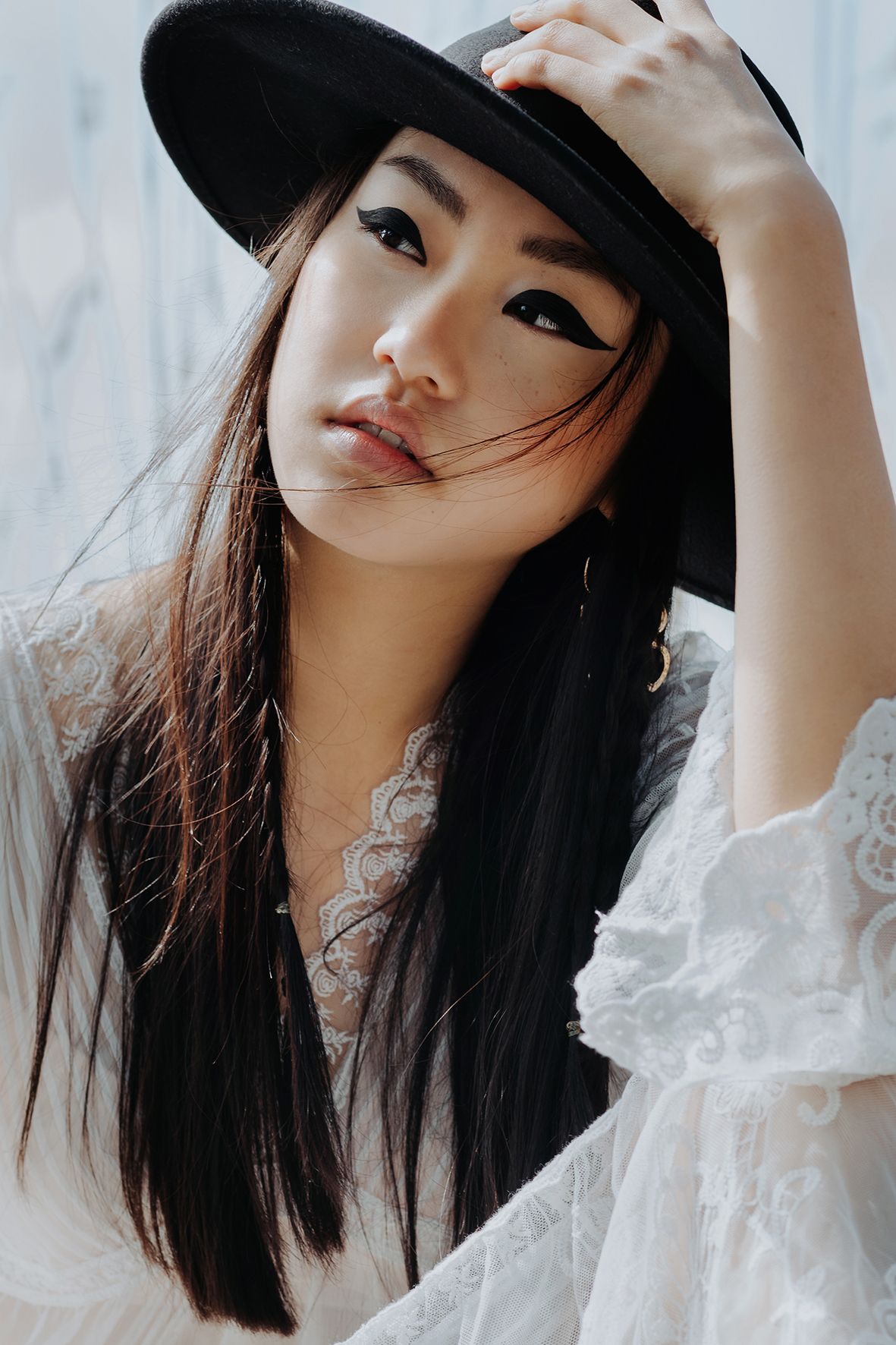 asian young girl with dark long hair and hat sitting near water and holding her hat