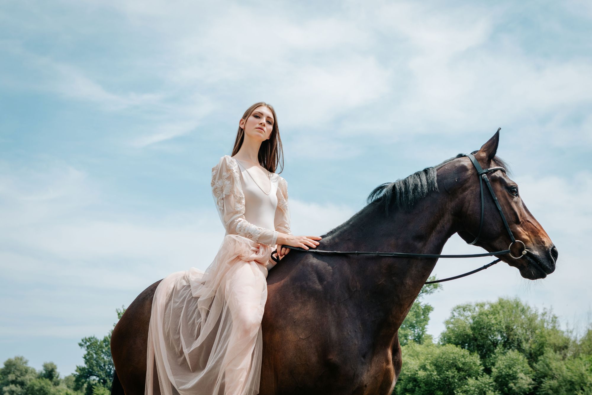 Girl with tulle dress sitting on a black horse with blue sky background